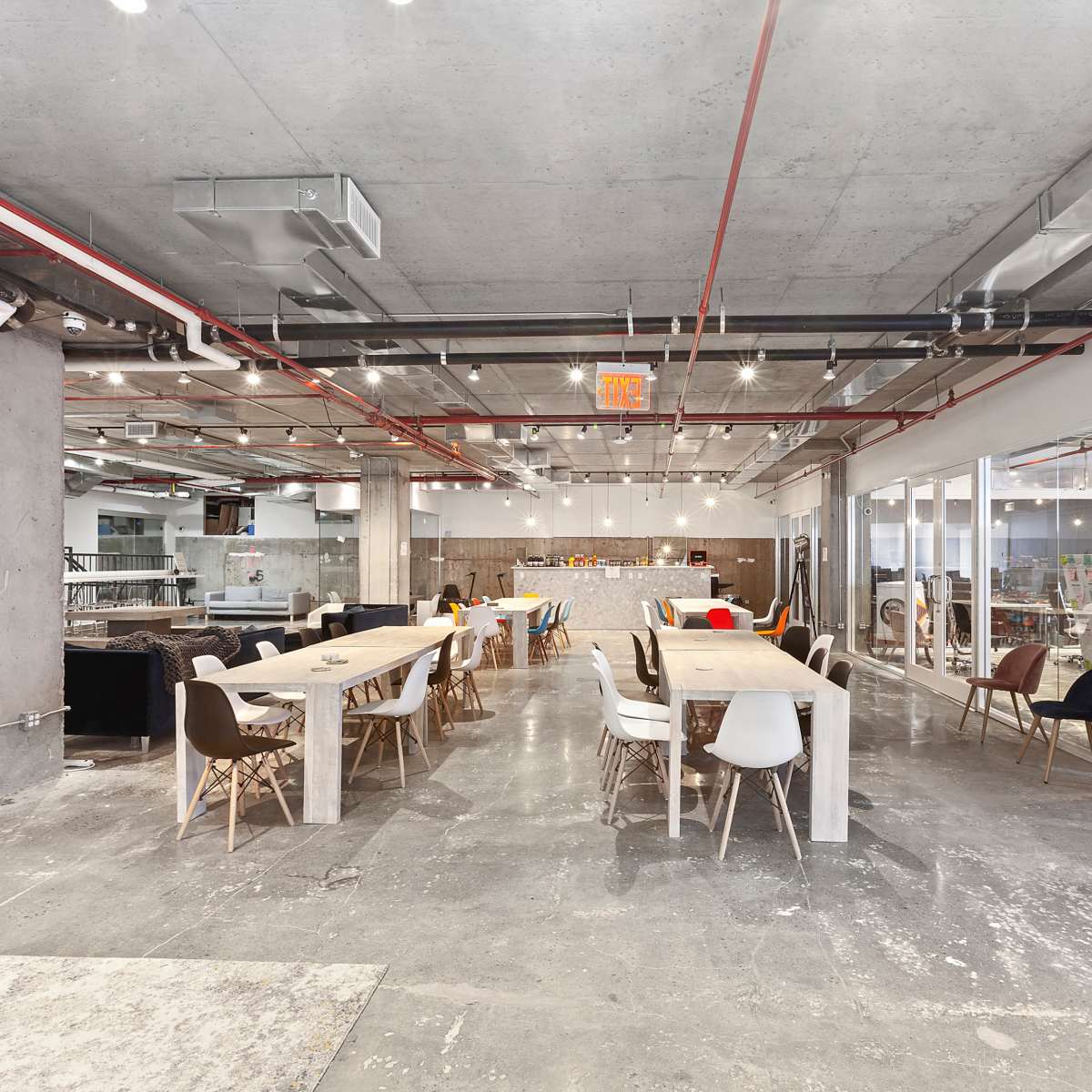 A spacious, modern office interior with long tables, various chairs, and industrial-style concrete walls and ceilings.