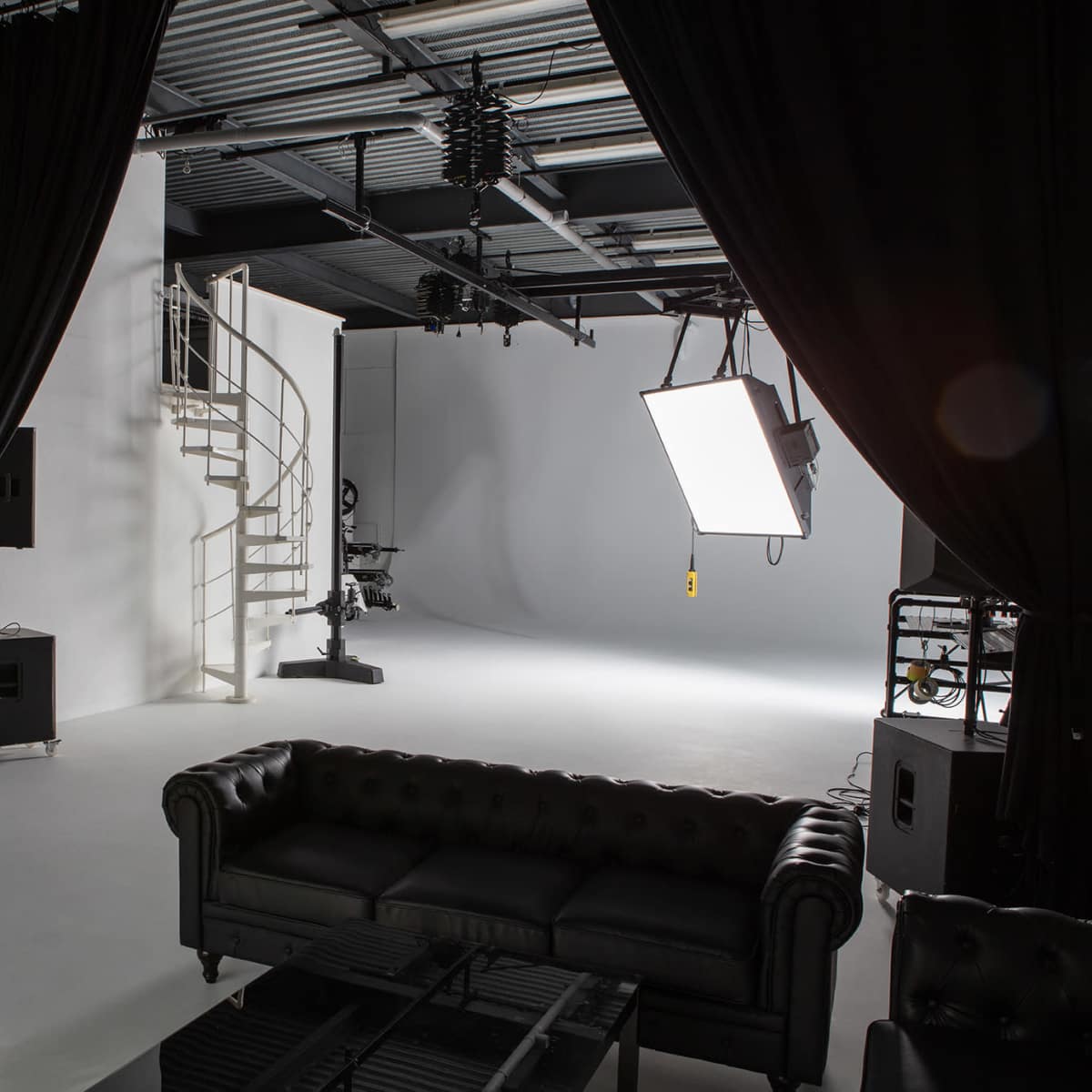 A photography studio equipped with a spiral staircase, lighting set-up, and a black couch.