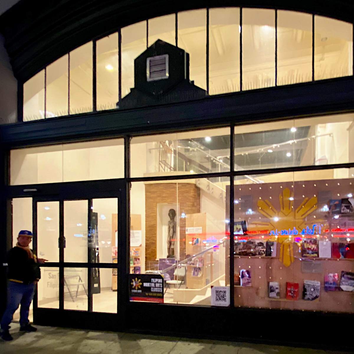 A person stands by a glass entrance of a building with visible signage and displayed items inside.