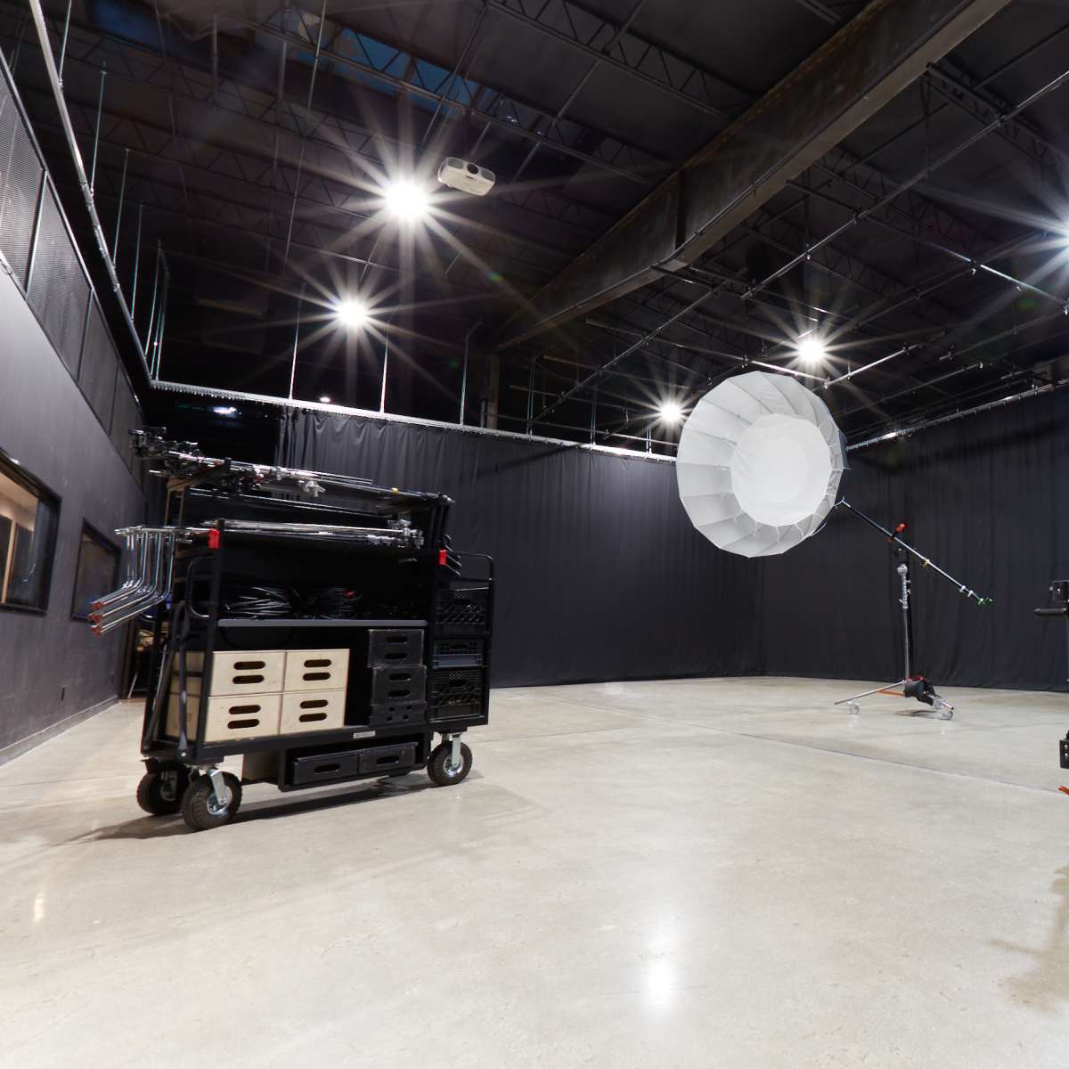 A photography studio featuring a large softbox on a stand, mobile equipment carts, and black backdrop curtains.
