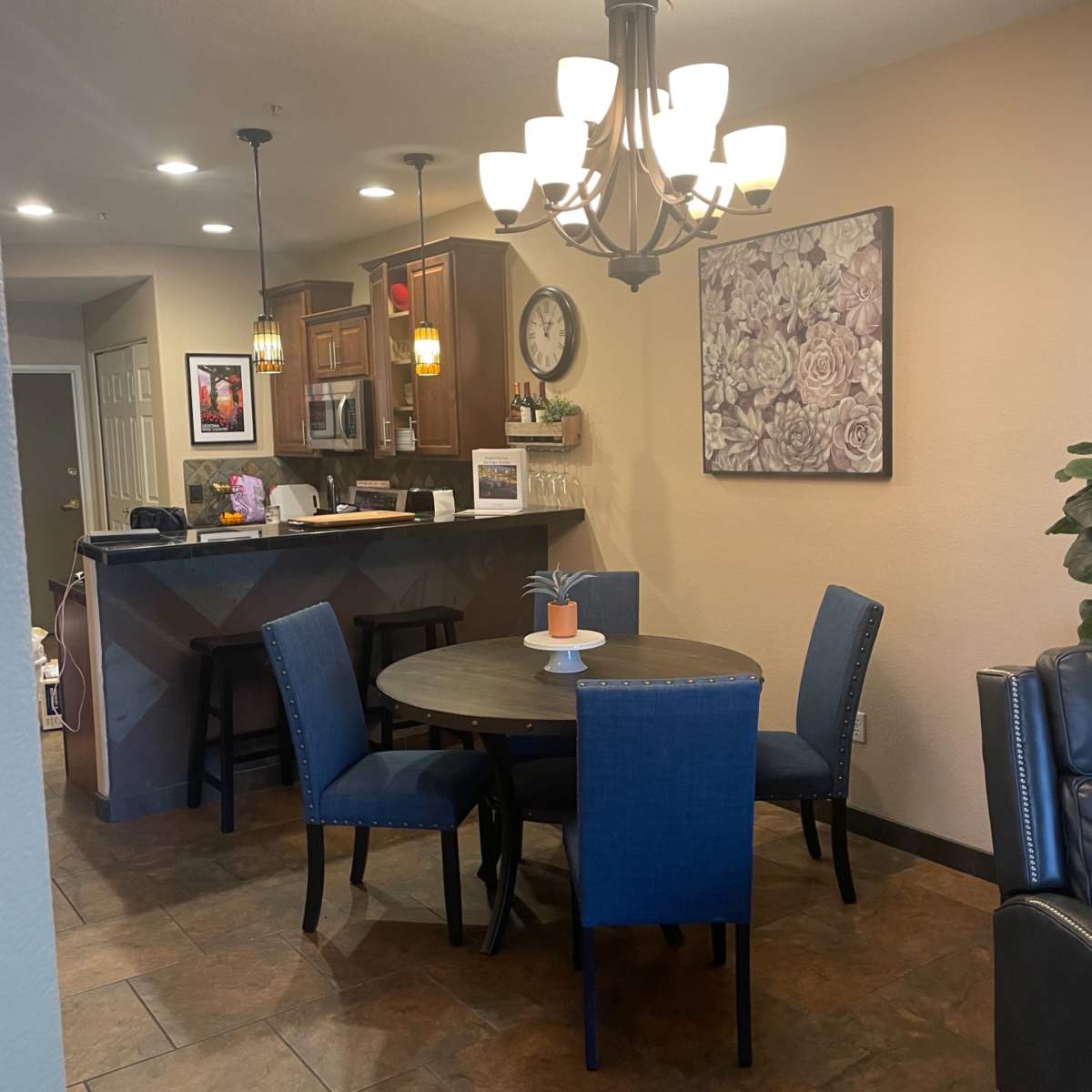 A dining area with a round table and four blue chairs, adjacent to a kitchen and inviting living space.