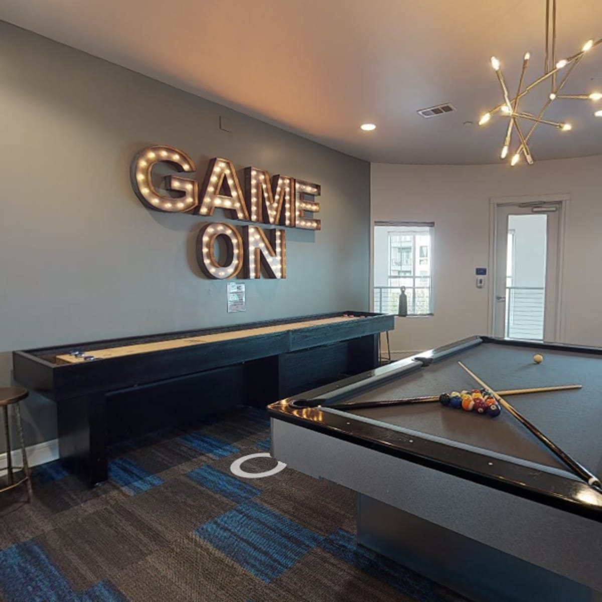 A recreational room featuring a pool table and a shuffleboard table, with a "GAME ON" sign illuminated on the wall.