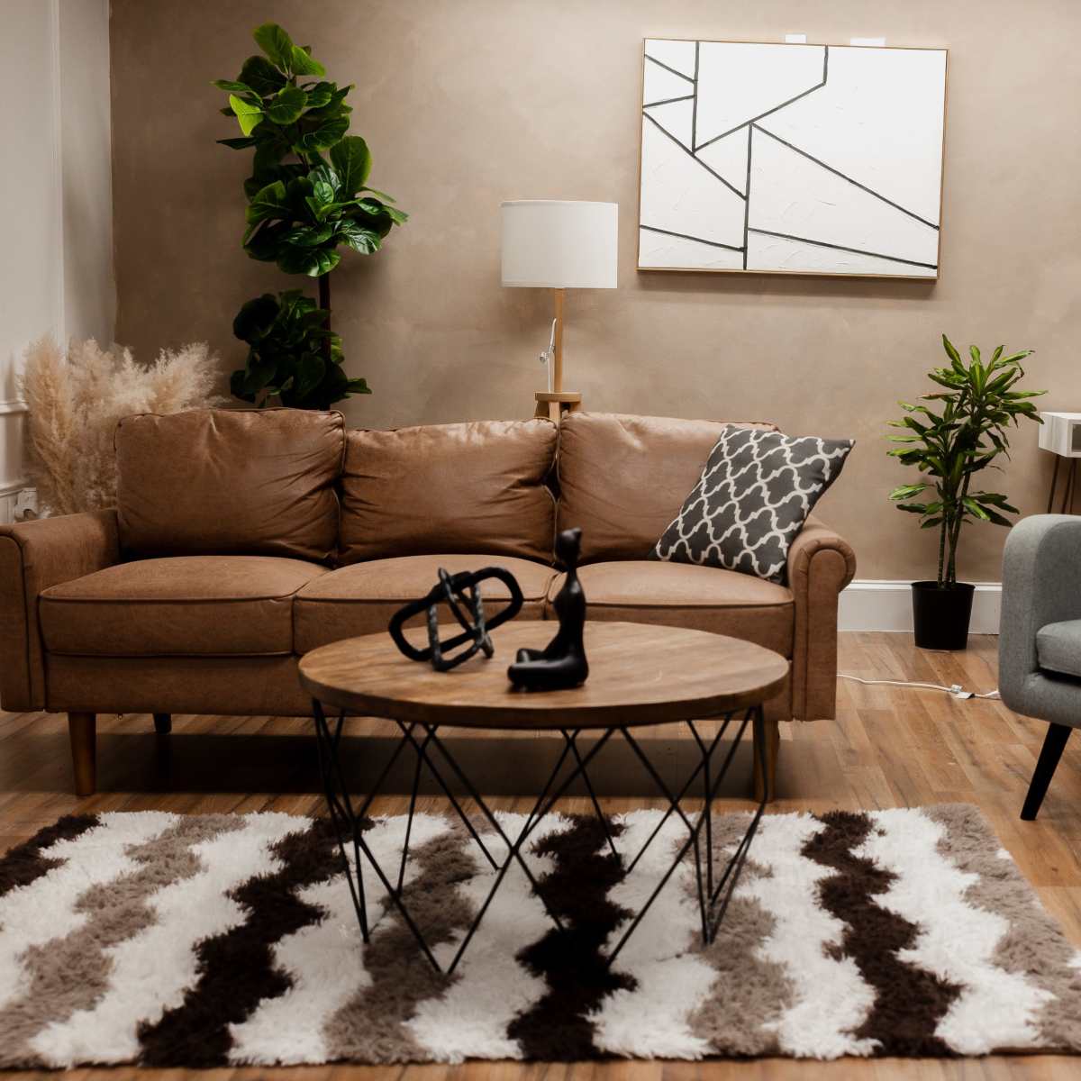 A stylish living room with a brown sofa, a gray armchair, a round wooden coffee table, and a decorative rug featuring a zigzag pattern.
