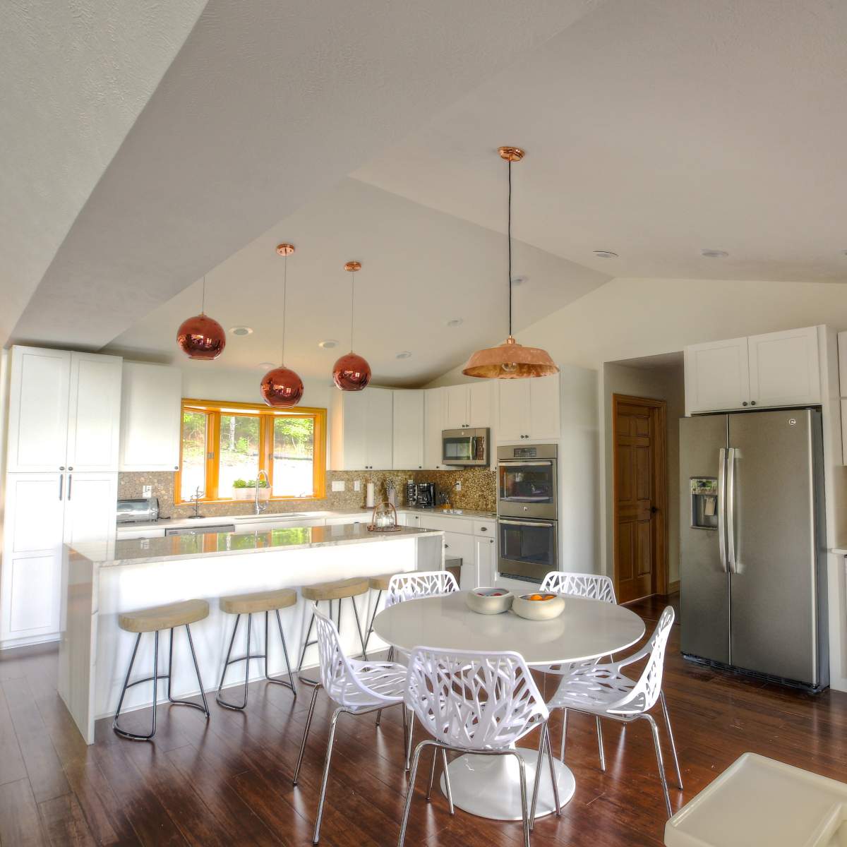 A modern kitchen features white cabinetry, stainless steel appliances, a large island with bar stools, and a dining table surrounded by stylish chairs.