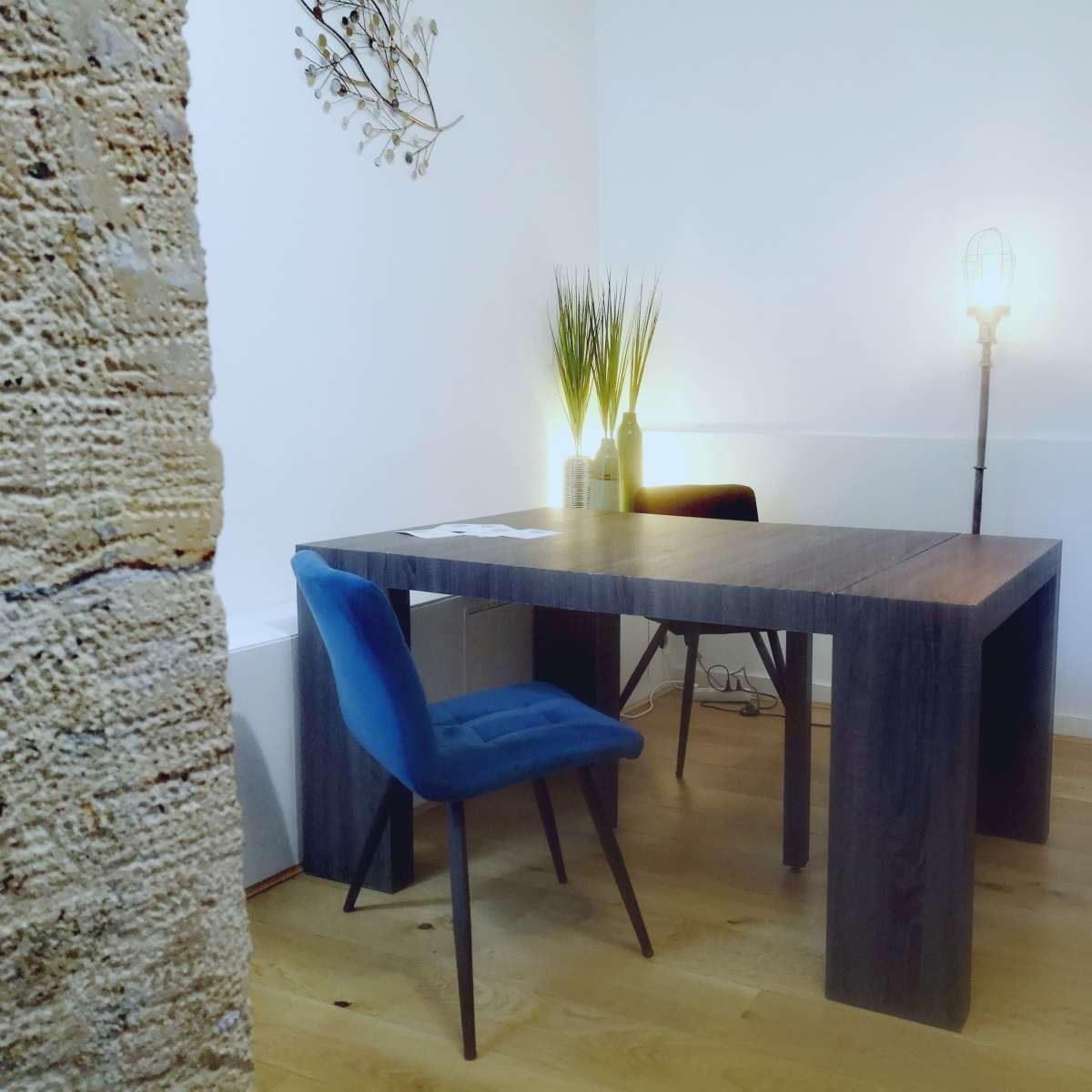 A simple office space with a wooden table, two chairs, and a small shelf containing decorative items.