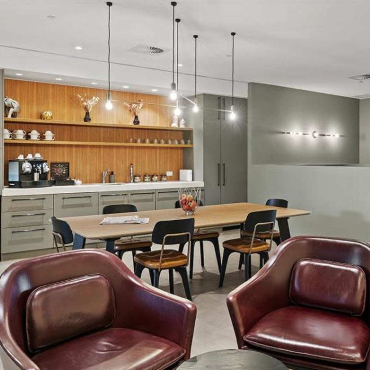 A modern office kitchen area featuring a wooden counter, a dining table, and several seating options, with appliances and refreshments readily available.