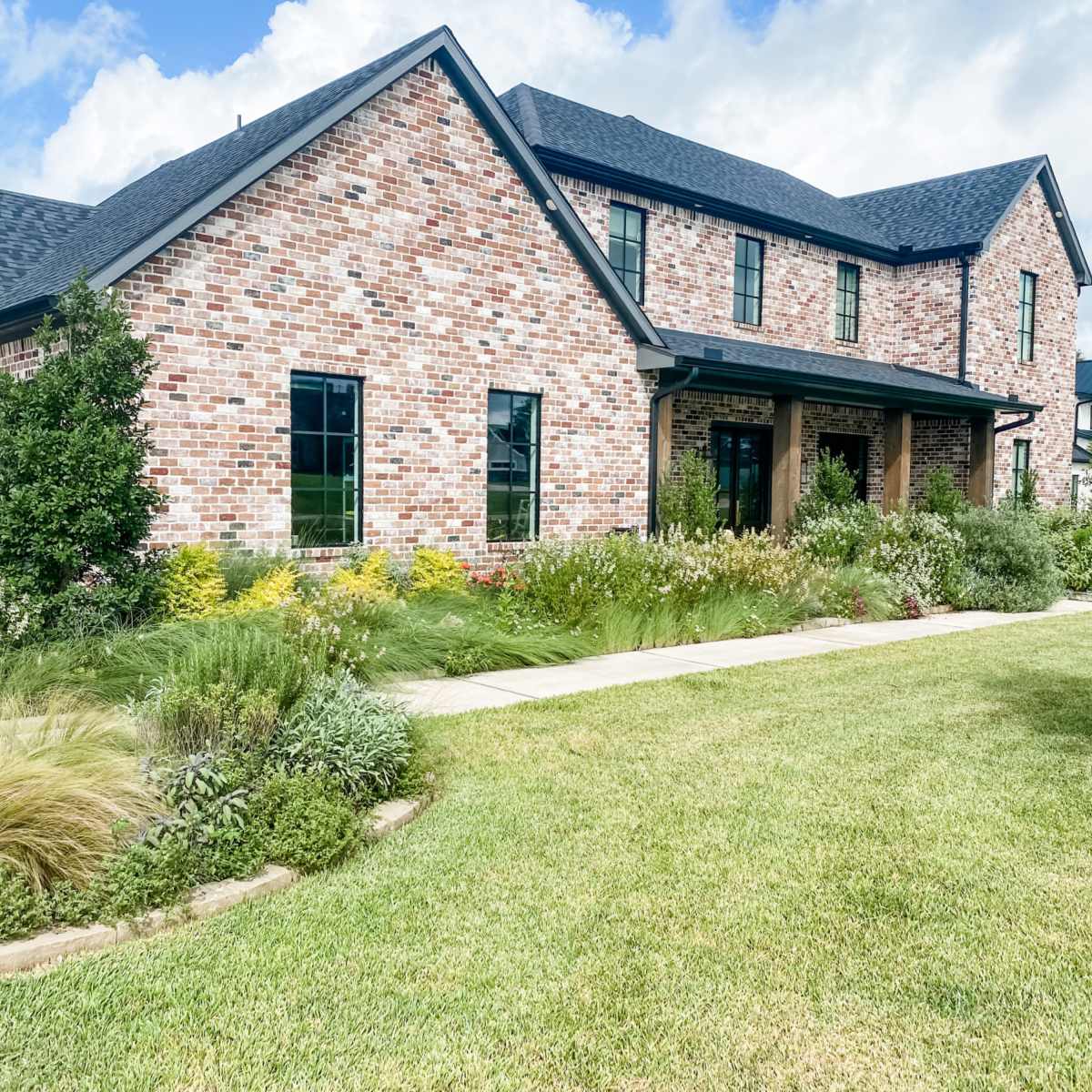 A two-story brick house with a landscaped yard featuring various plants and a walkway leading to the entrance.