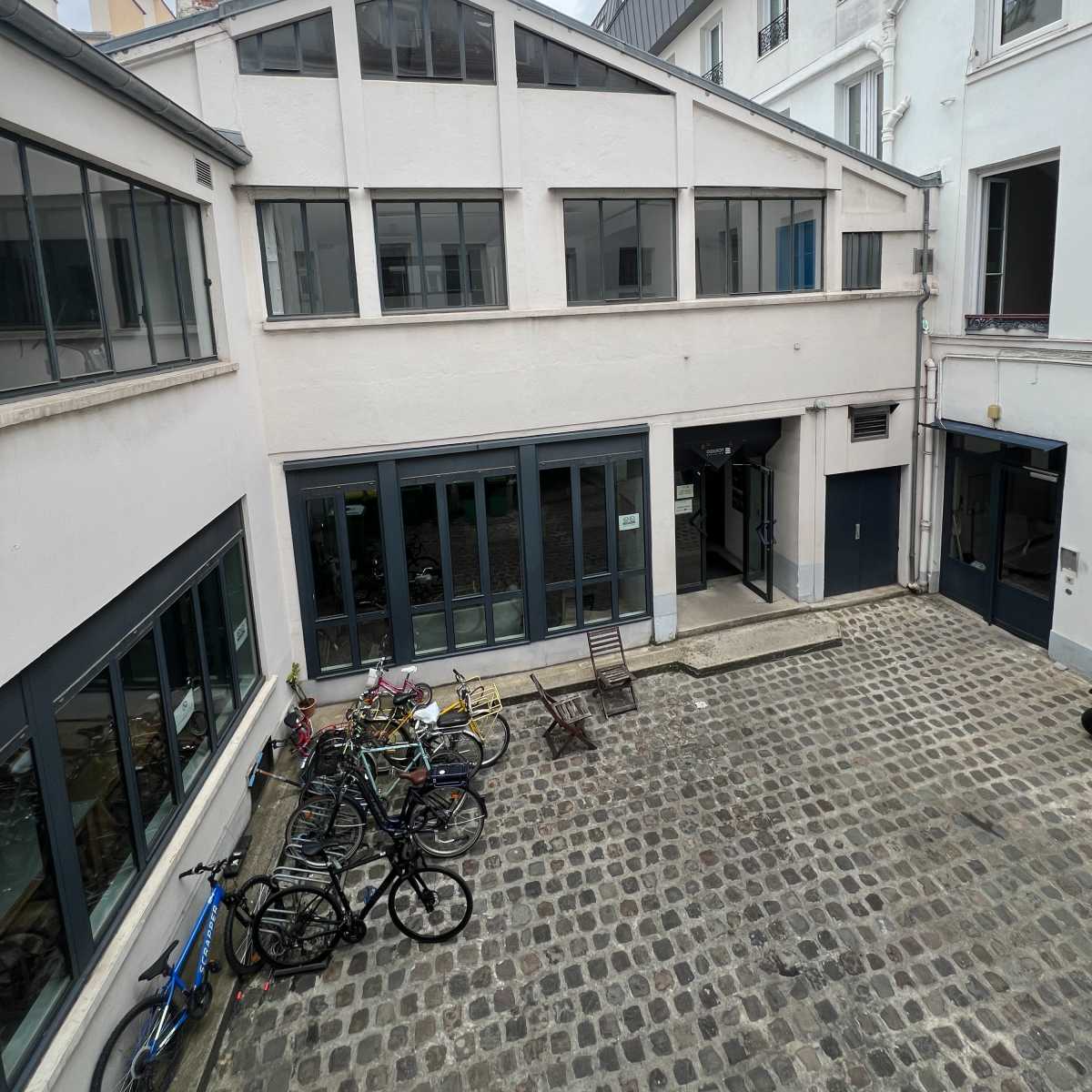 A cobblestone courtyard surrounded by white buildings with large windows and several parked bicycles.