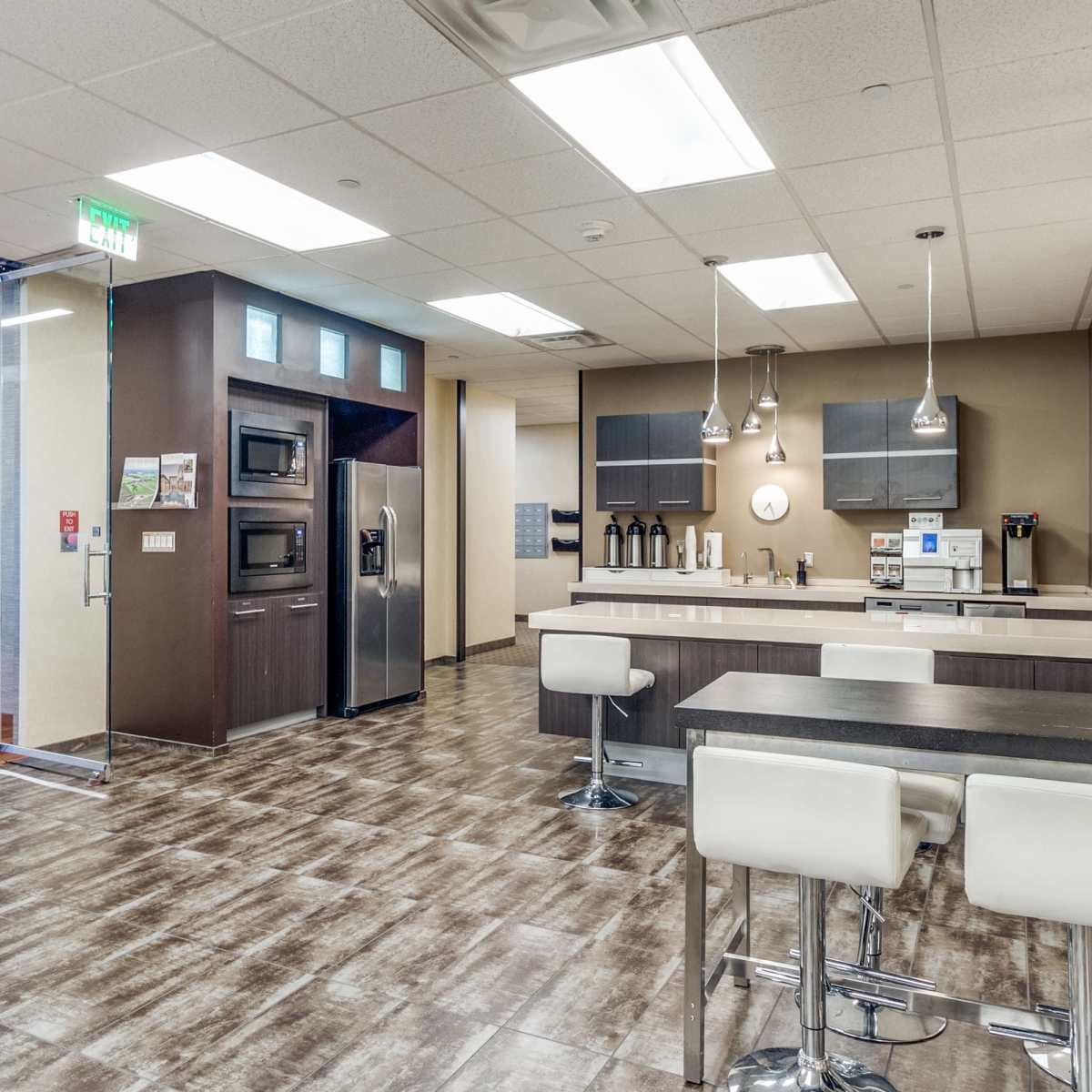 A modern kitchen area with a dining table and seating, adjacent to an elevator lobby.