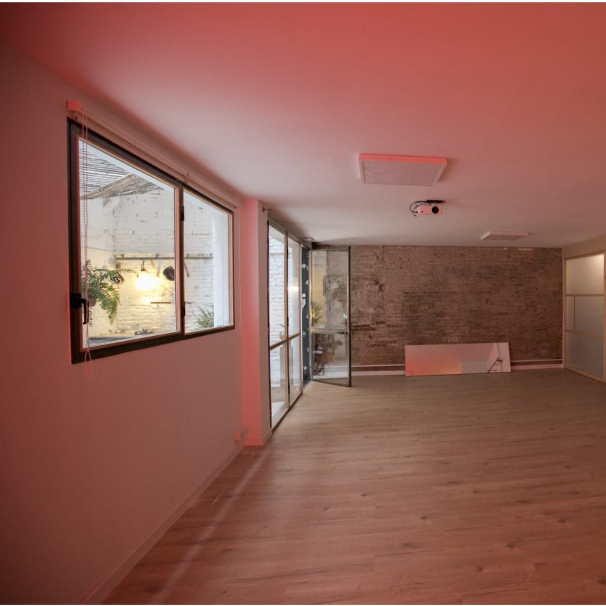 A spacious, minimalistic room with wooden flooring, a brick wall, large windows, and a guitar hanging on the wall.