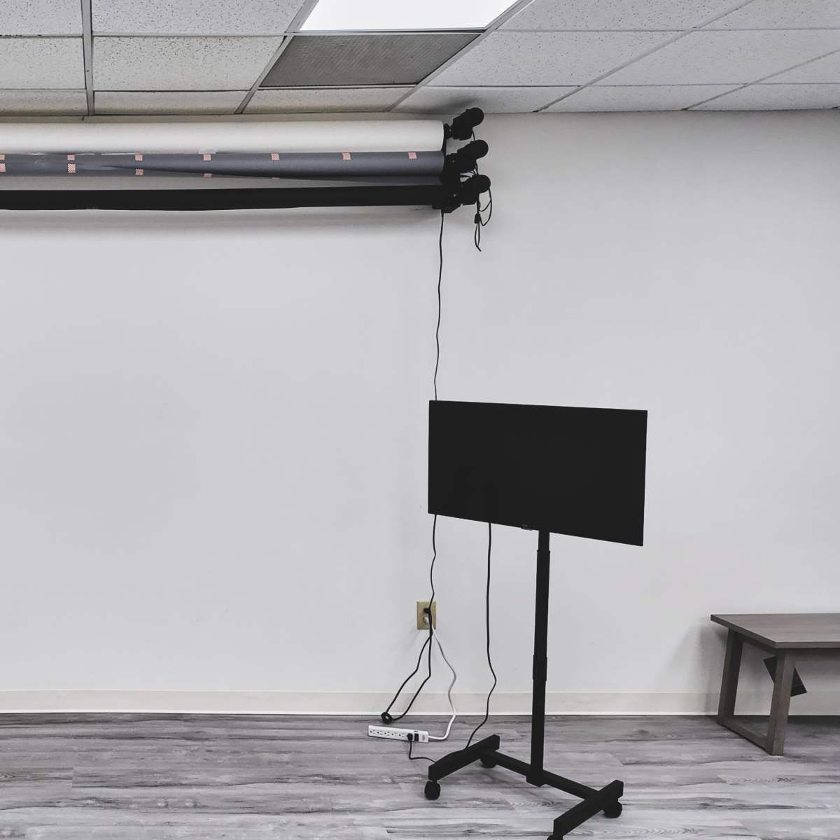 A bare room with a wall-mounted backdrop system and a small TV stand beside a wooden stool.