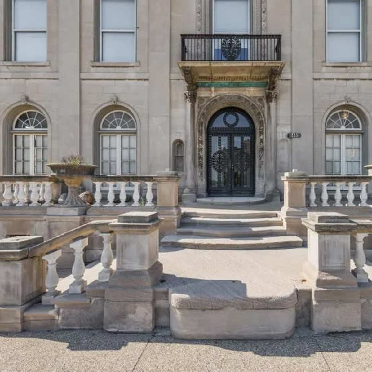 The grand entrance of a large stone building featuring a staircase with a railing and decorative planters on either side.