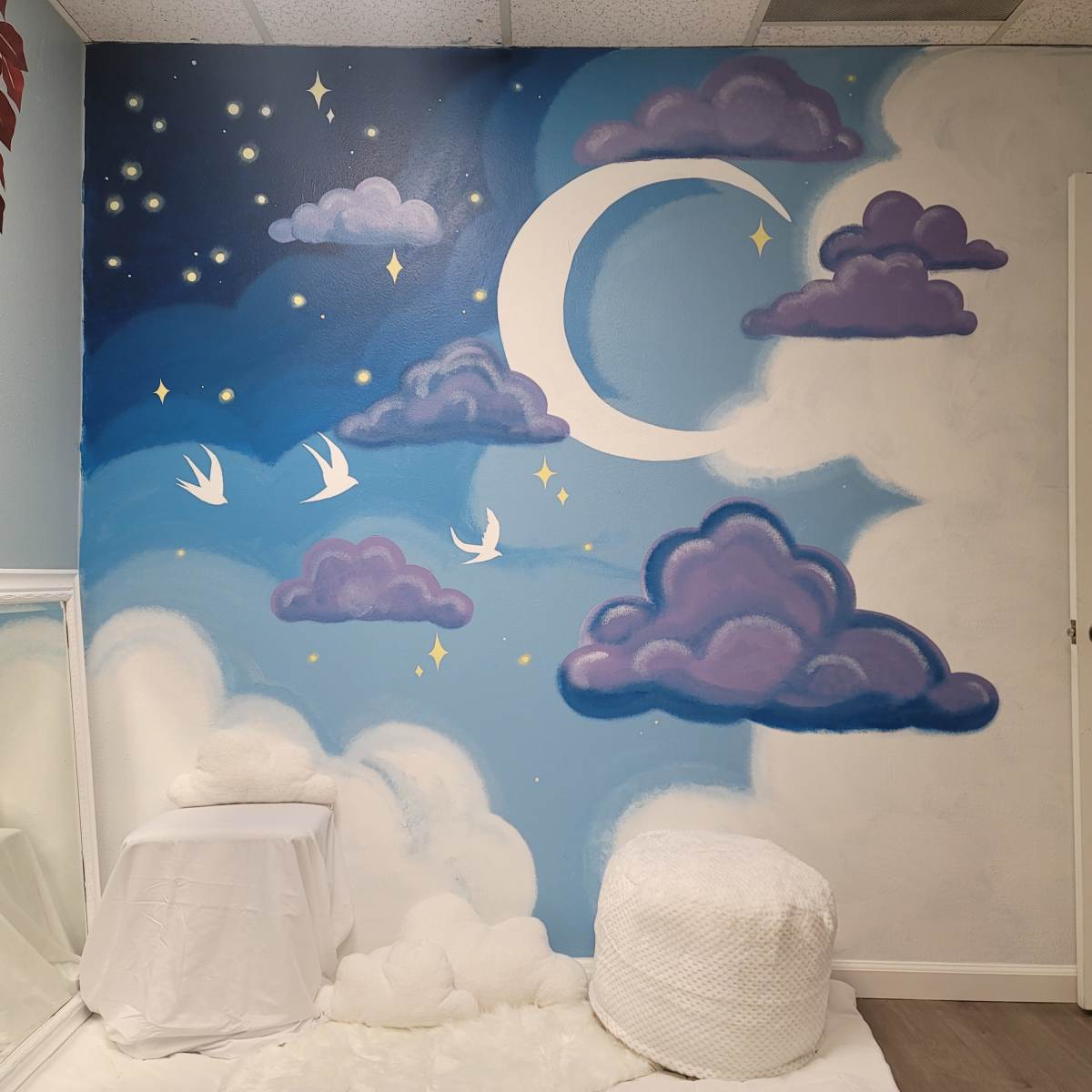 A mural of a crescent moon and clouds painted on a wall, accompanied by flying birds and stars.