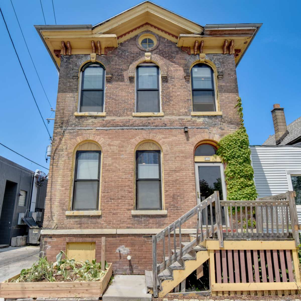 A three-story brick building with large windows, a staircase leading to the entrance, and vines climbing one side.