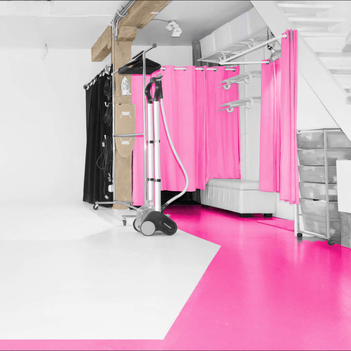 A photo studio with a white backdrop, pink flooring, and various props including black and pink curtains.