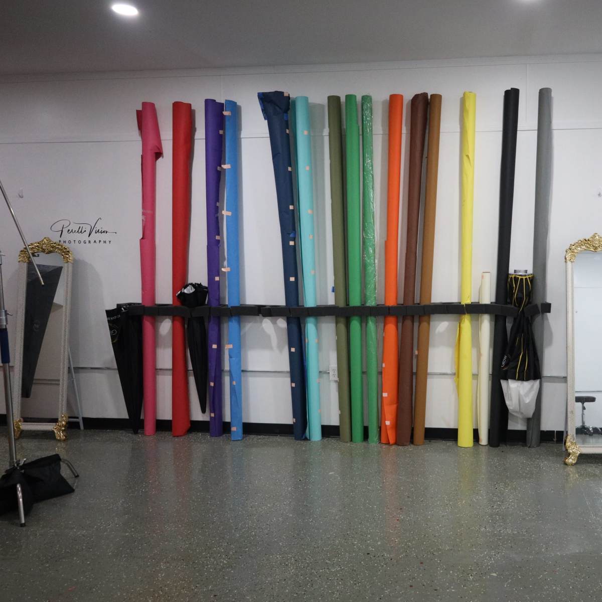 A studio space with colorful backdrop rolls on a wall, a full-length mirror, and a bouquet of flowers displayed nearby.