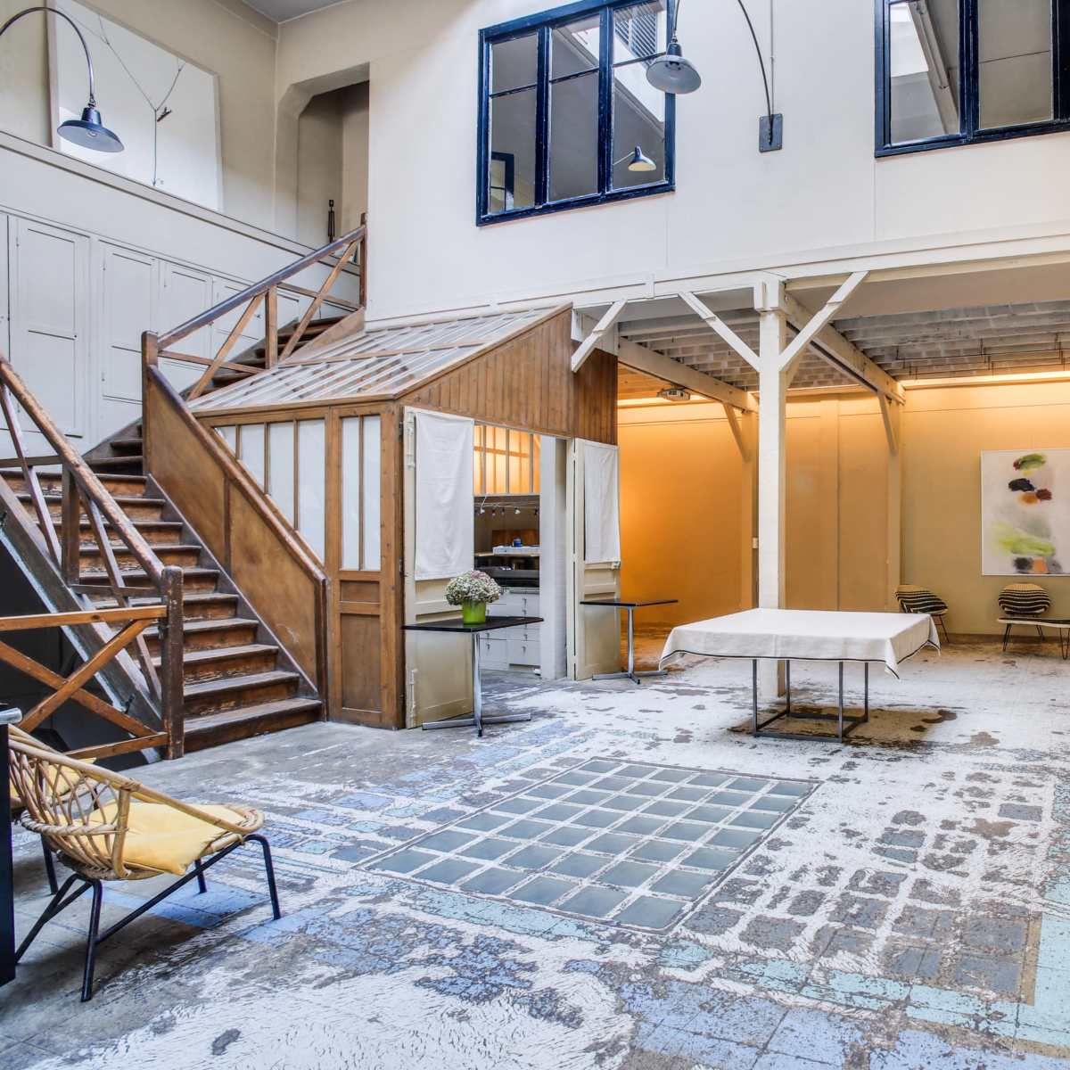 A spacious, industrial-style interior with a staircase, seating area, and large windows allowing natural light to enter.