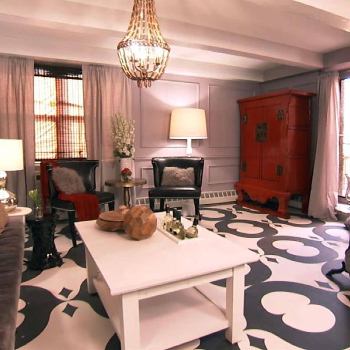 A living room featuring a gray tufted sofa, a white coffee table, an ornate orange cabinet, and two black chairs, all arranged around a patterned floor.