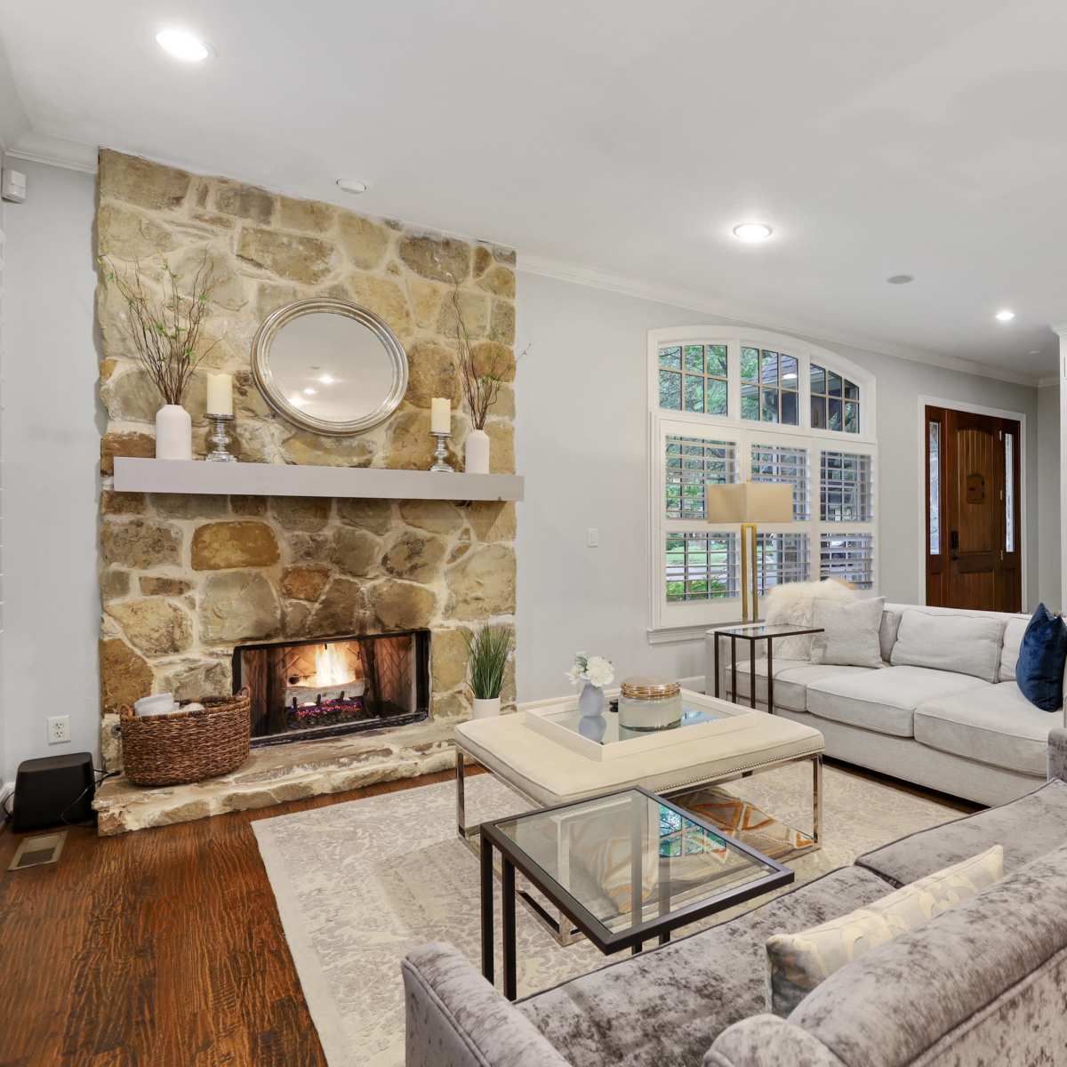 A living room with a stone fireplace, comfortable seating, and a coffee table, all arranged in a well-lit space with decorative photographs on the wall.