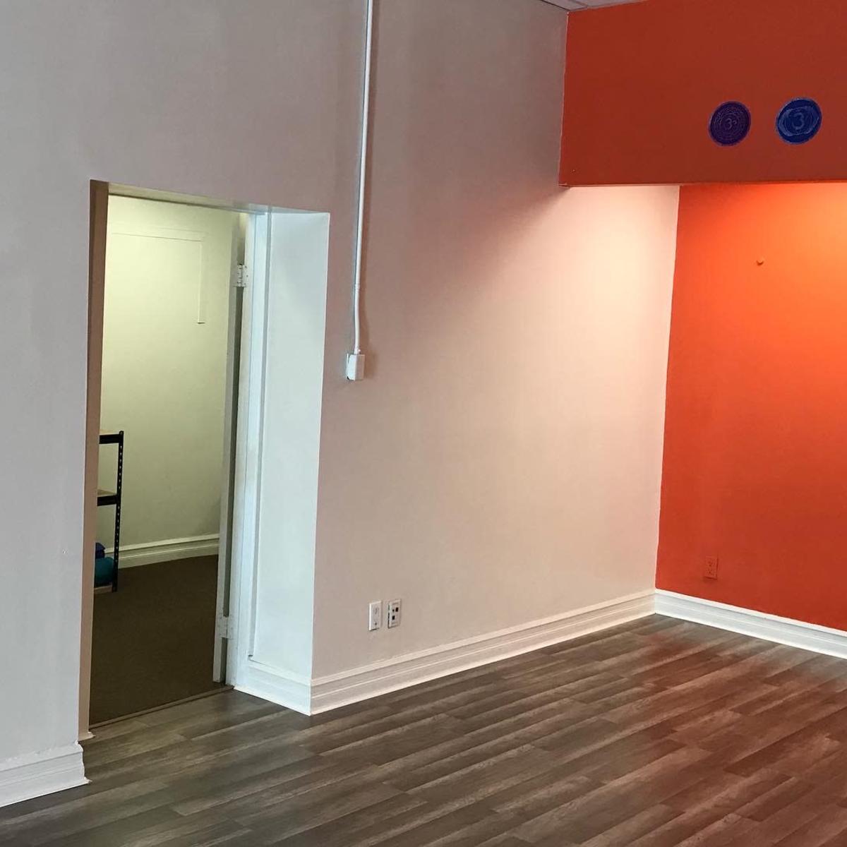 A room with a wood floor and a partially open doorway leading to another room, featuring an orange accent wall.