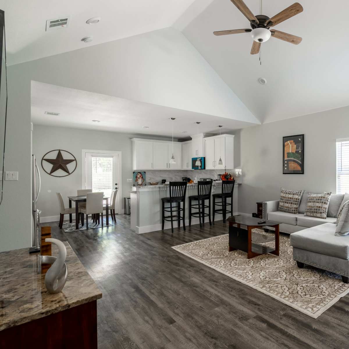 A modern living room with a sectional sofa, a coffee table, and a view into a kitchen with bar stools and dining area.