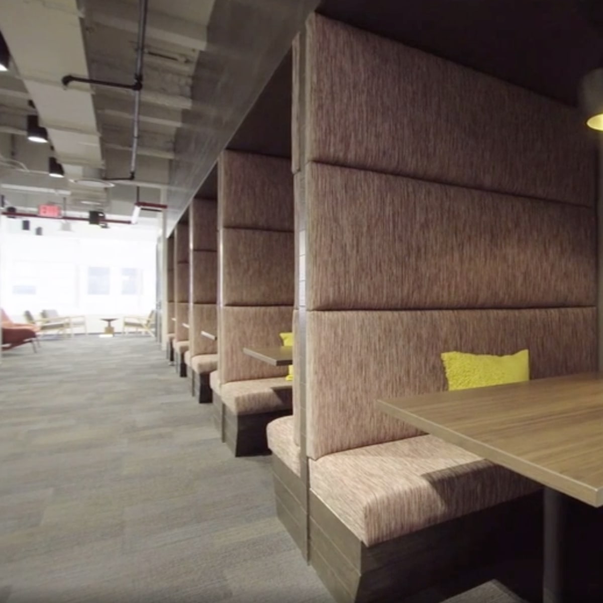 A modern office space with cozy seating areas featuring tall upholstered walls, wooden tables, and pendant lighting.