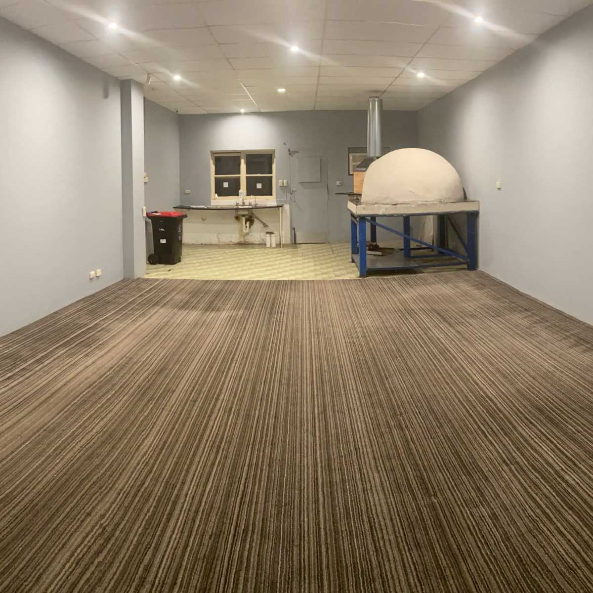 A wide, empty room with gray walls, a patterned carpet, and a round structure on a blue table at the far end.
