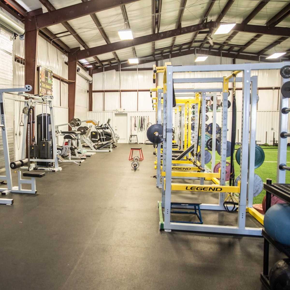 An indoor gym filled with various weightlifting equipment and workout machines arranged along the walls of a large, open space.