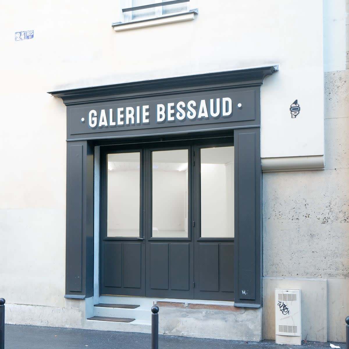 The entrance of a gallery named "Galerie Bessaud," featuring a dark facade and large glass doors, set against a plain building wall.