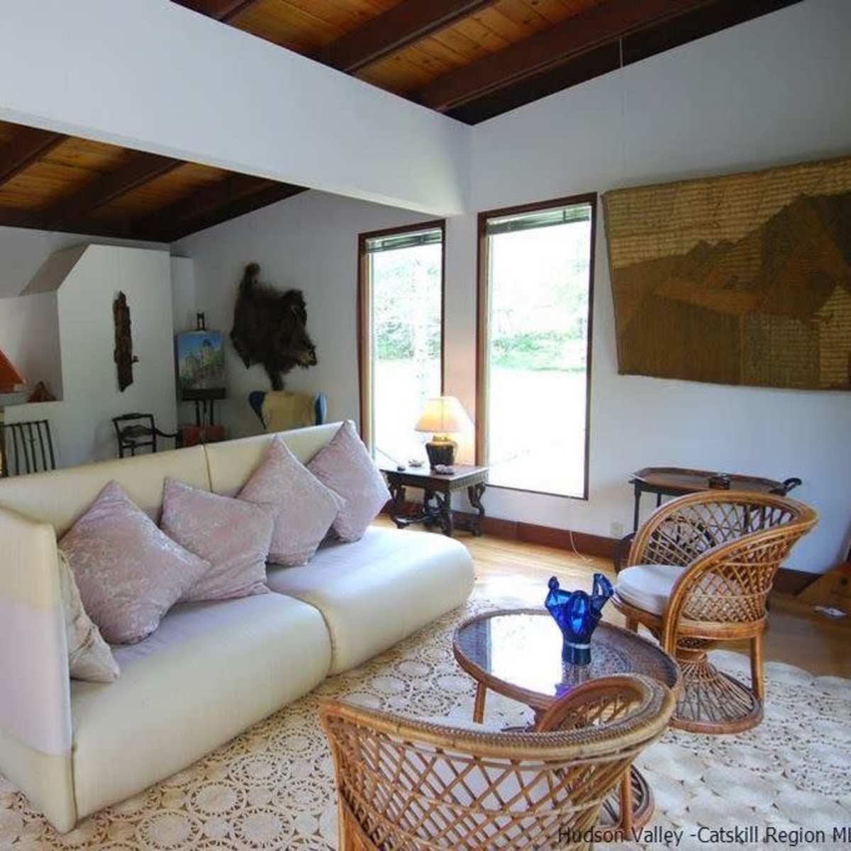 A spacious living room with a white sofa, a wooden ceiling, a large fireplace, and natural light streaming through multiple windows.