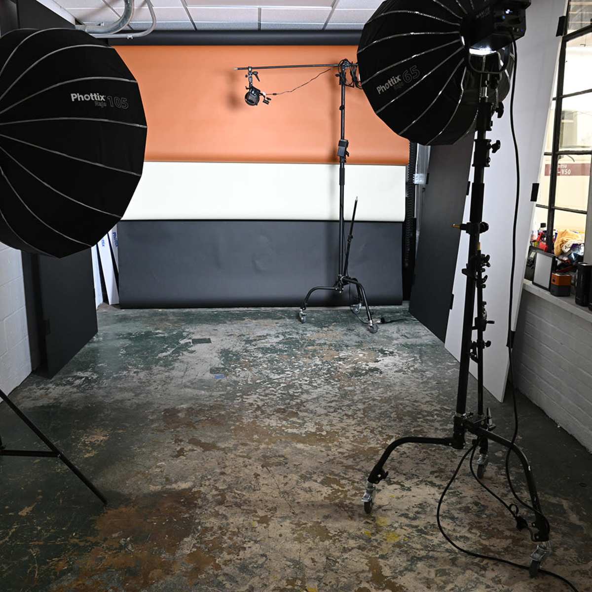 A photography studio setup with two large softbox lights on stands, an orange and black backdrop, and a worn concrete floor.