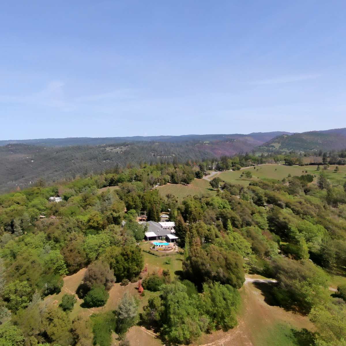 Aerial view of a lush, green landscape featuring a residential area amidst rolling hills and trees.