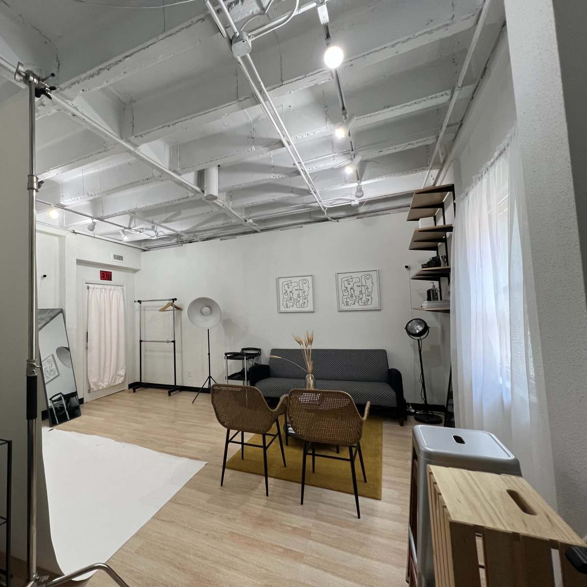 A spacious photo studio with a white backdrop, seating area, and various lighting equipment arranged around the room.
