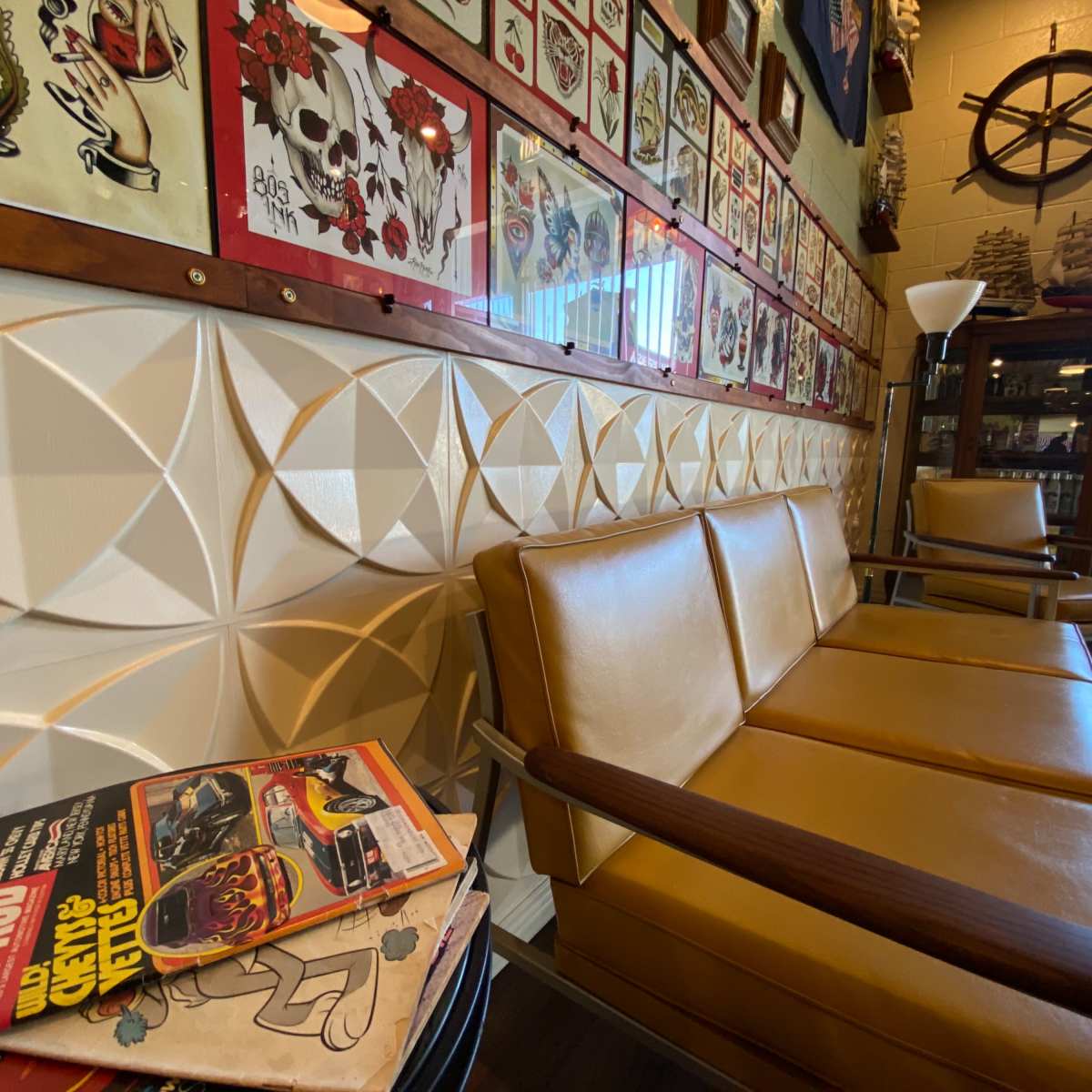 A vintage-style seating area with a textured wall, adorned with framed art, and a stack of magazines resting on the floor.