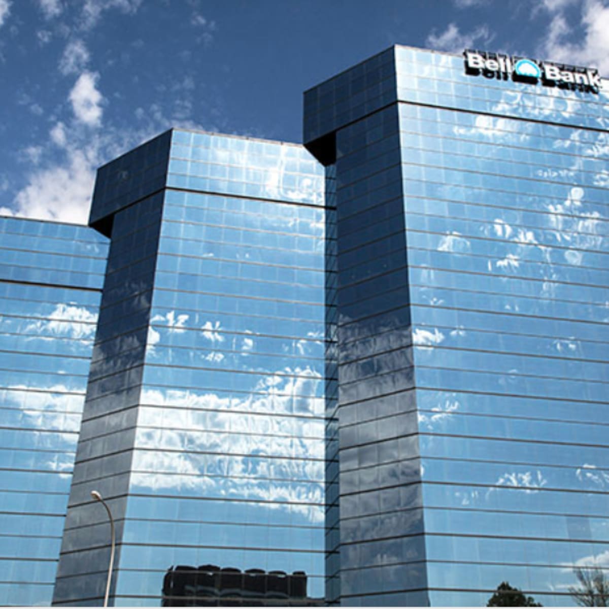 A tall, glass-covered building with a sign reading "Bell Bank" reflects the sky and surrounding landscape.