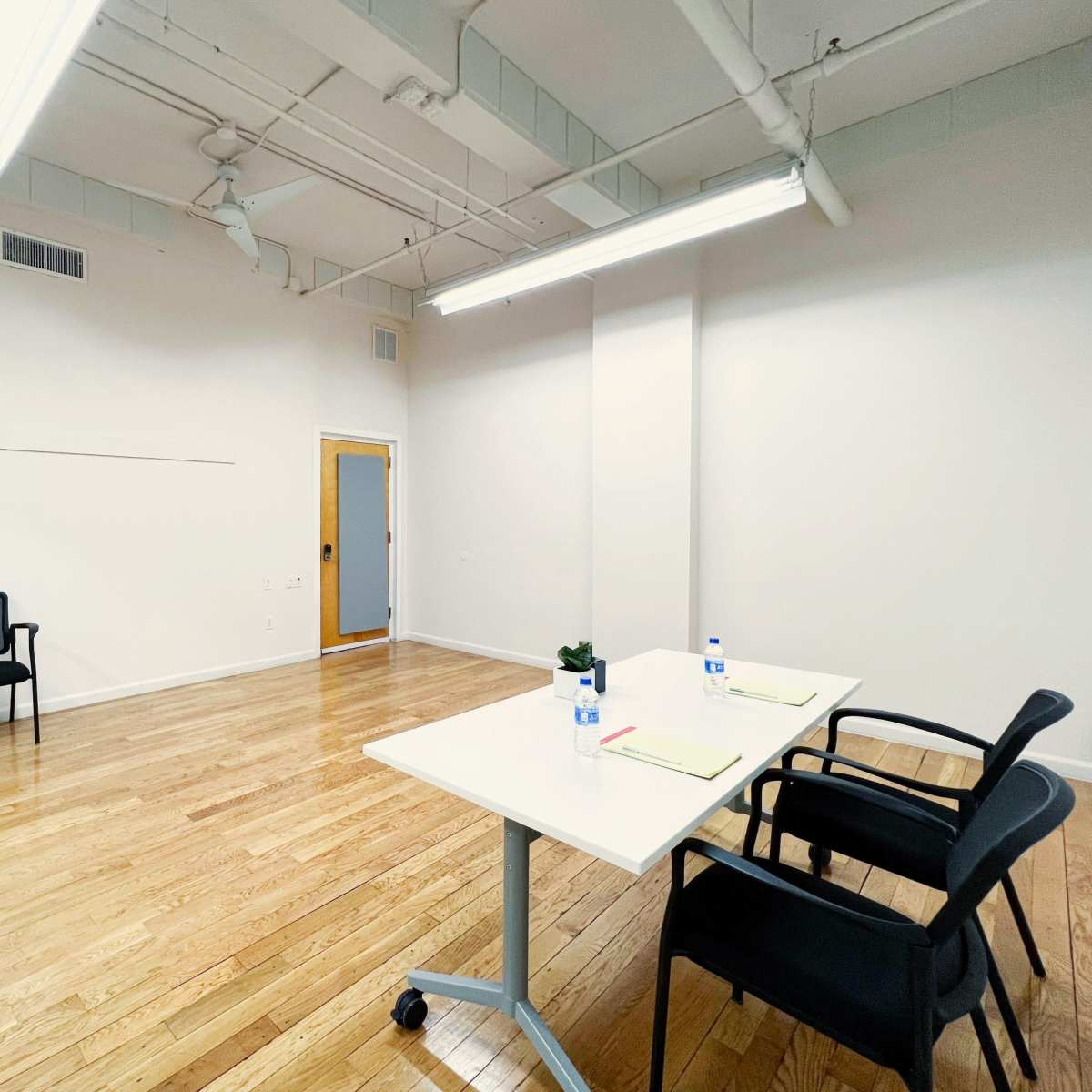 A nearly empty room with a table and chairs, featuring wooden floors and white walls.