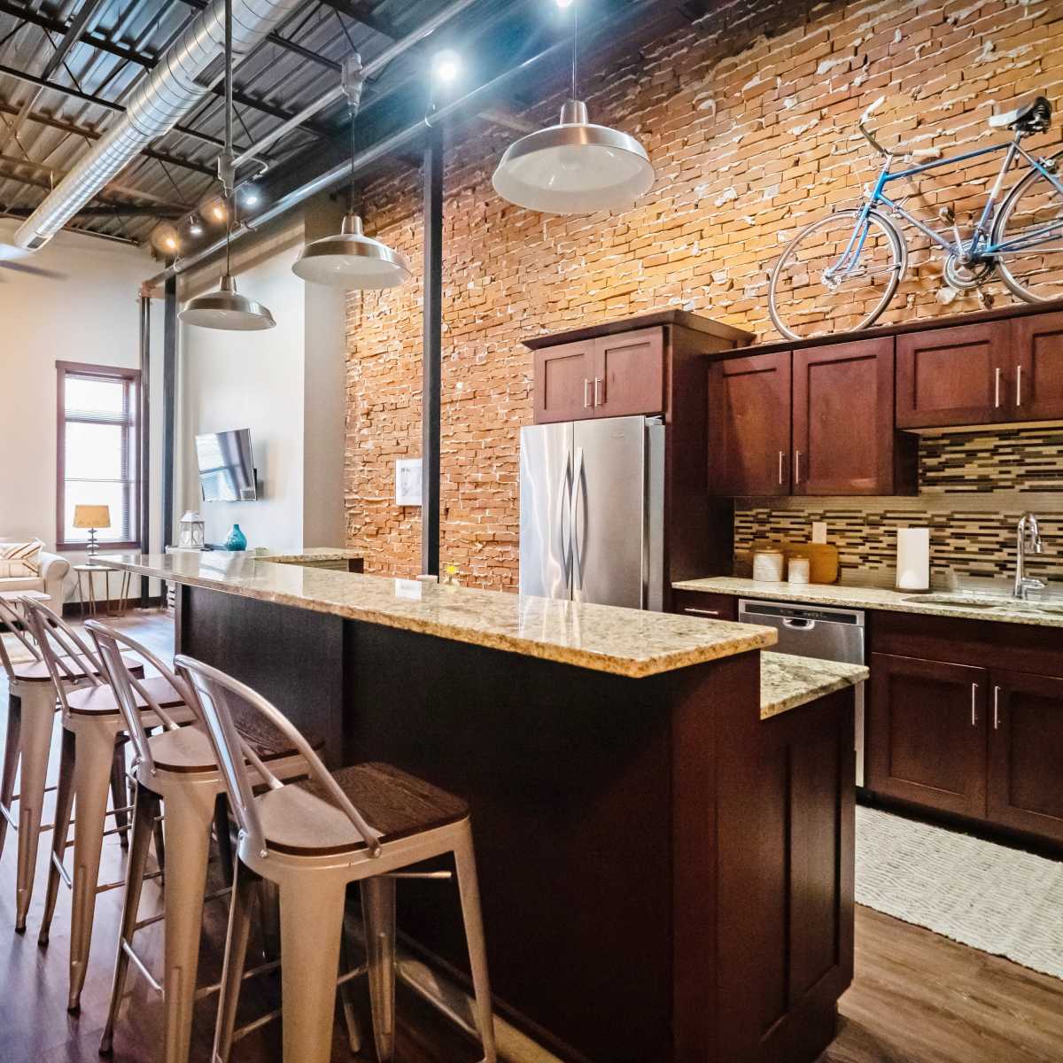 A modern kitchen with granite countertops and dark wooden cabinetry, accented by a brick wall and a bicycle mounted above the cabinets.