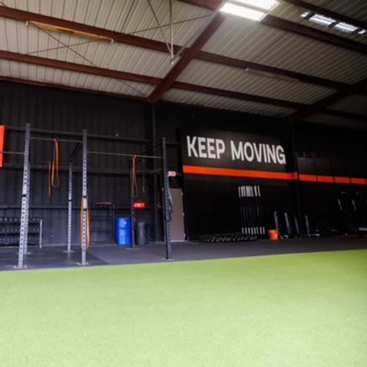 A gym interior with workout equipment, including weights and a pull-up rig, alongside a motivational slogan on the wall.