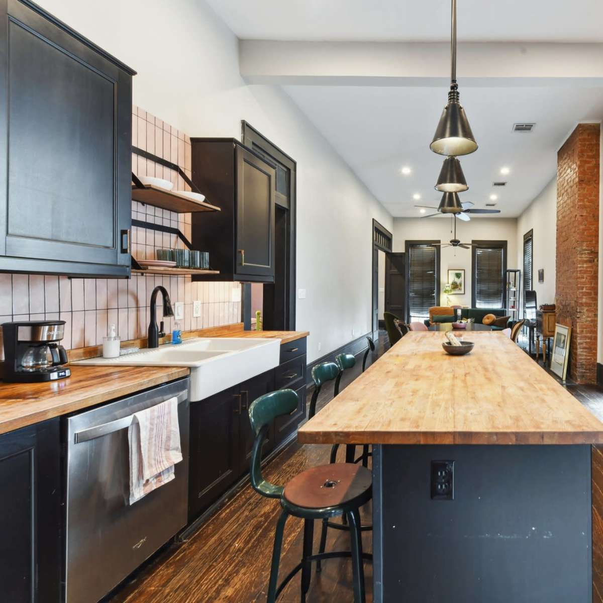 The kitchen features a long wooden island, black cabinetry, stainless steel appliances, and exposed brick walls.