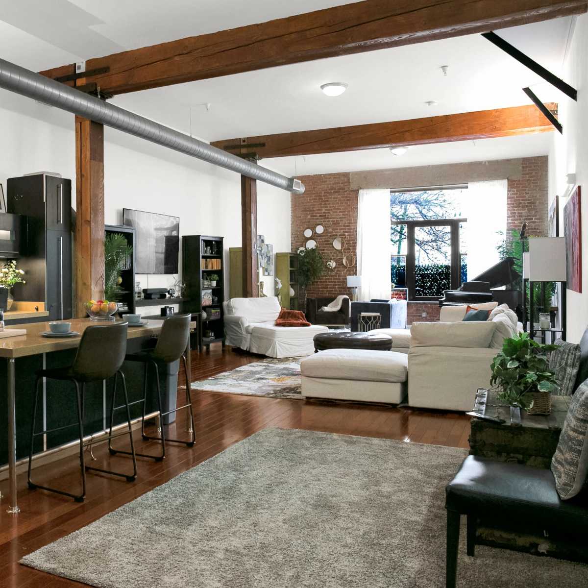 A spacious, open-concept living area featuring a kitchen with a large island, modern appliances, a seating area with a sofa and armchair, and large windows allowing natural light to fill the room.