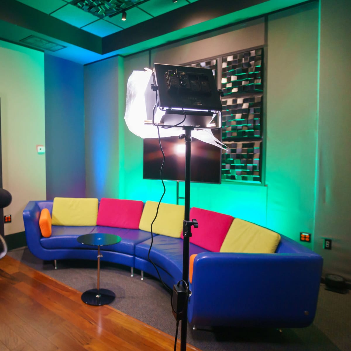 A modern studio setup featuring a colorful curved couch, a small black table, and professional lighting equipment against a backdrop with green and blue illumination.