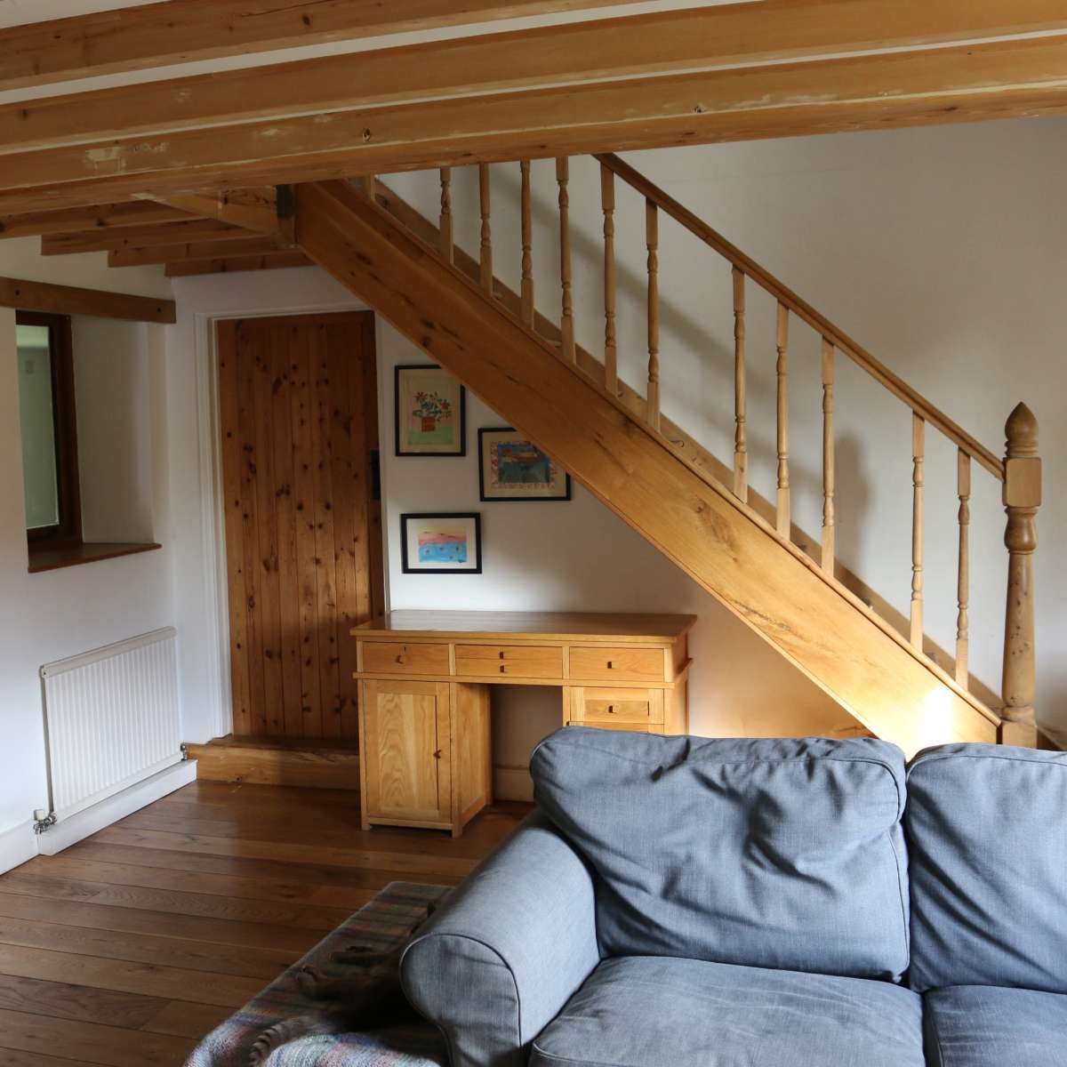 A living room featuring a wooden staircase, a desk, and a cozy couch, with framed artwork on the walls.