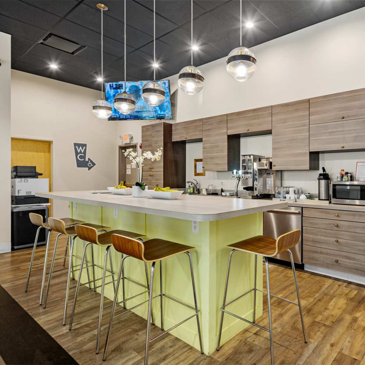 A modern kitchen with sleek cabinets, a long island with bar stools, and various appliances, including a refrigerator and microwave.
