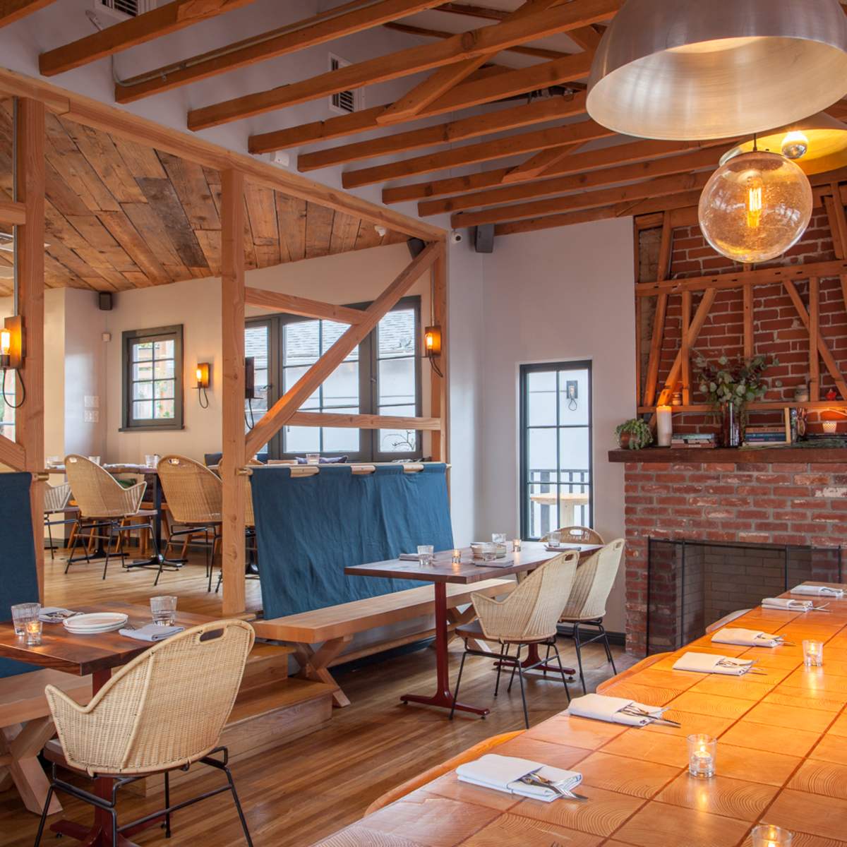 A restaurant interior featuring wooden beams, a brick fireplace, and tables set for dining.