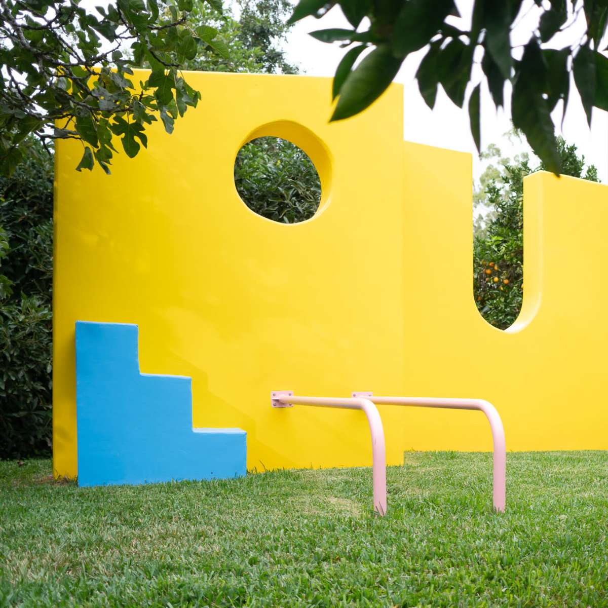 A vibrant yellow playground structure with a blue step, circular cutout, and swinging ropes set on a grassy area.