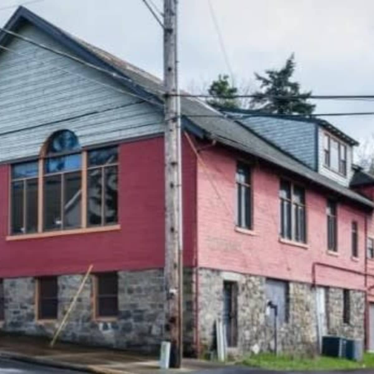A two-story red building with a stone base and large windows, situated at the corner of a street.