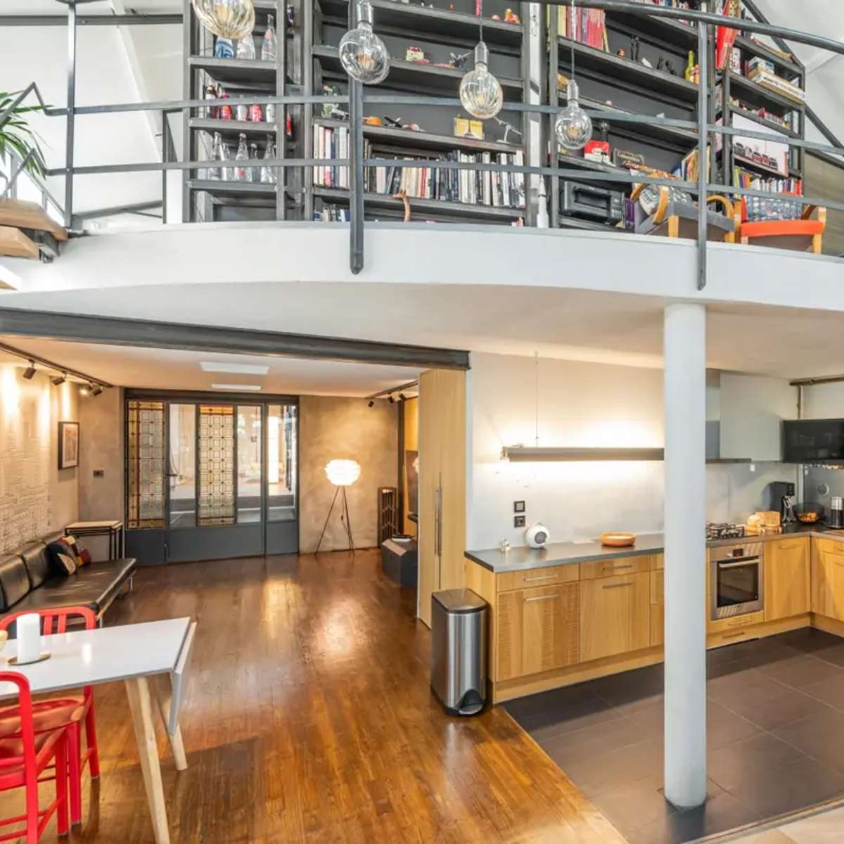 A modern, open-concept kitchen and living area with wooden floors, a kitchen island, and a spiral staircase leading to a lofted space filled with bookshelves.