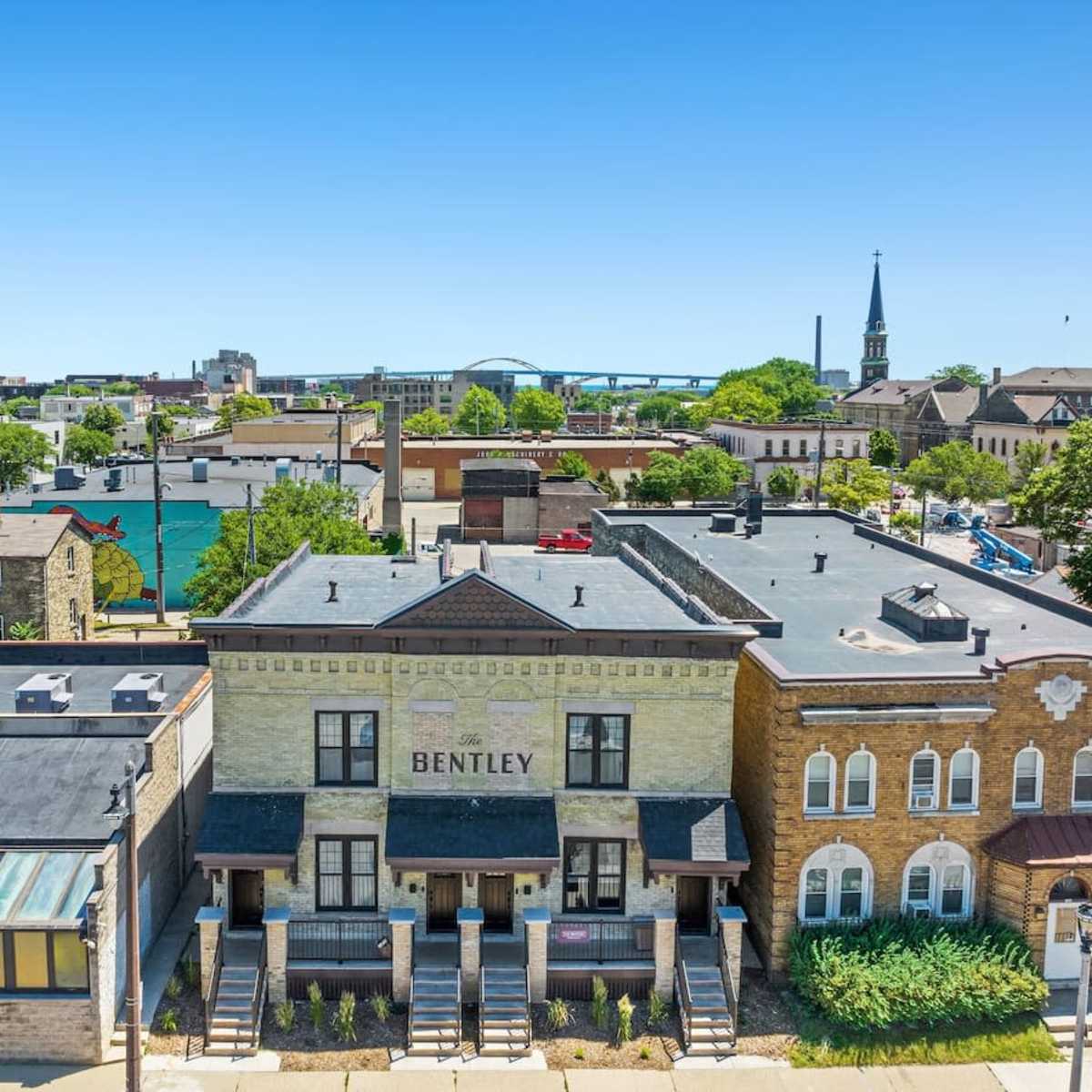 A view of a cityscape featuring the Bentley building, several surrounding structures, and a prominent steeple in the background.