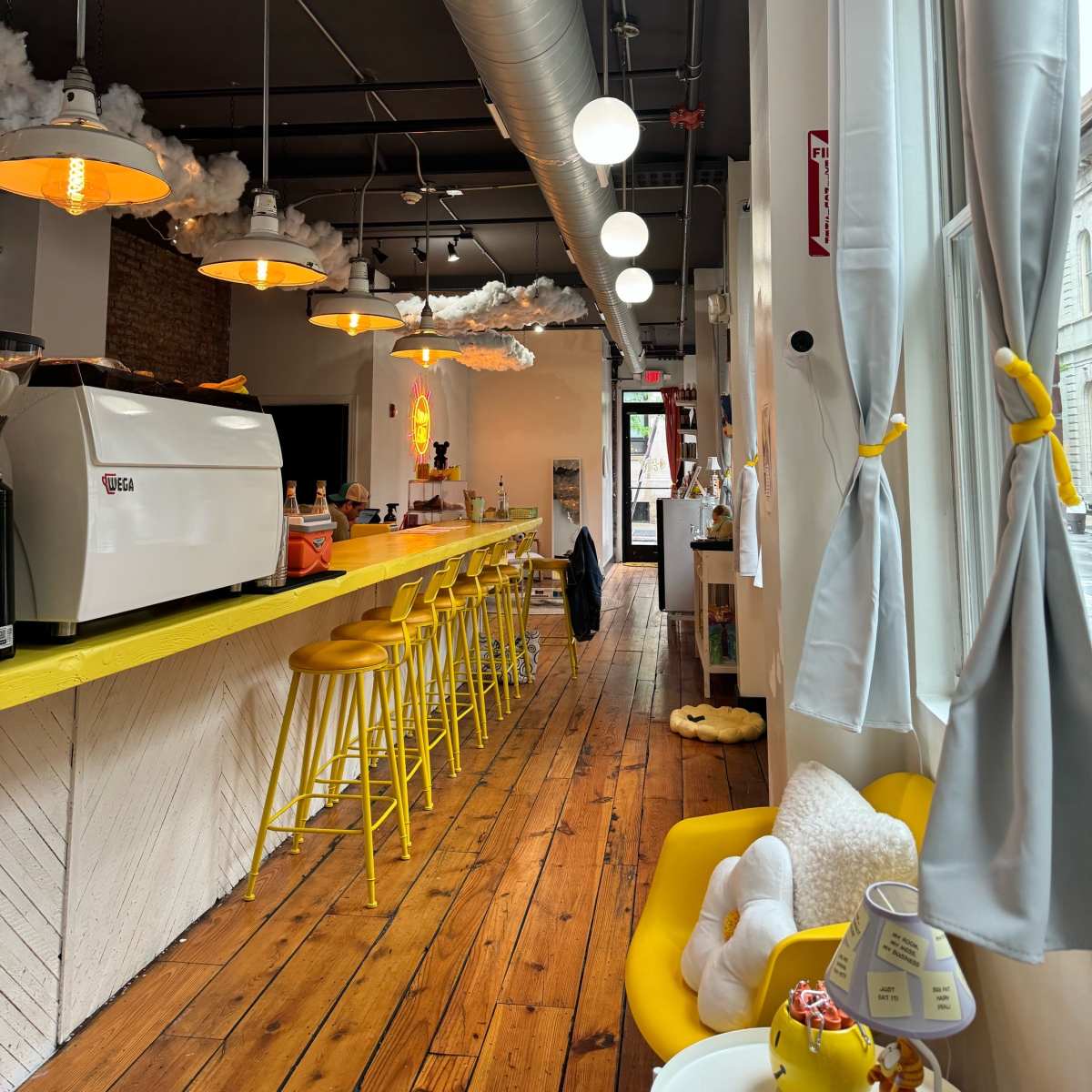 A modern café interior with yellow bar stools, a coffee machine, and light fixtures hanging from the ceiling.