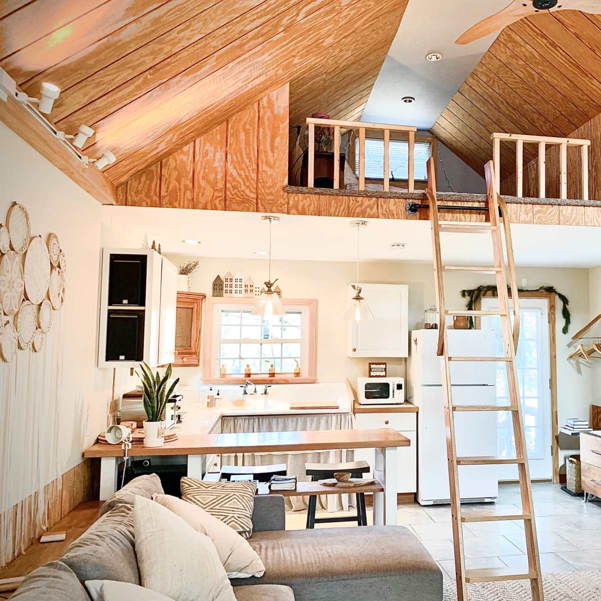A cozy living space featuring a loft area, wooden beams, a kitchen with a small island, and a staircase leading to the loft.
